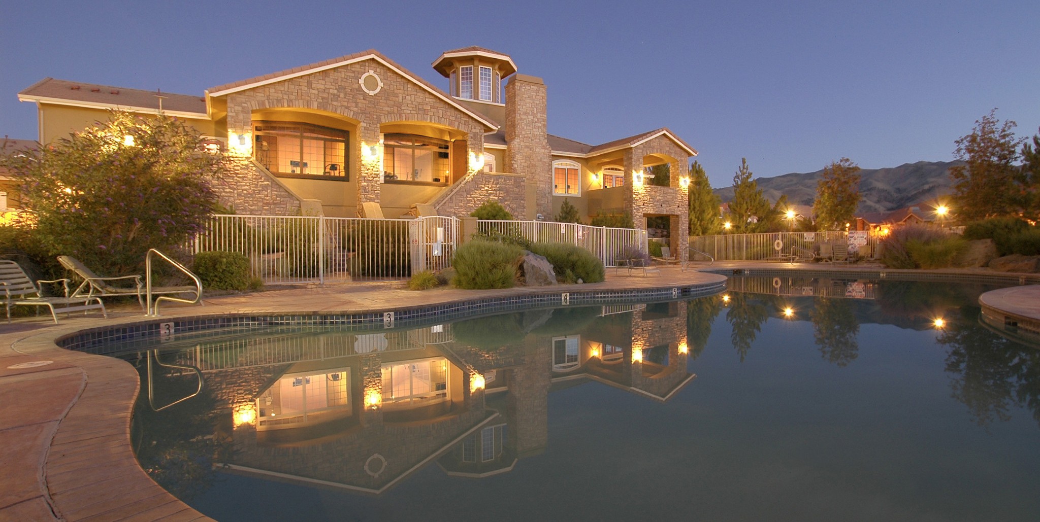 View of Aviana's clubhouse in the evening with the pool in the foreground. The illuminated clubhouse is reflected in the waters of the pool.