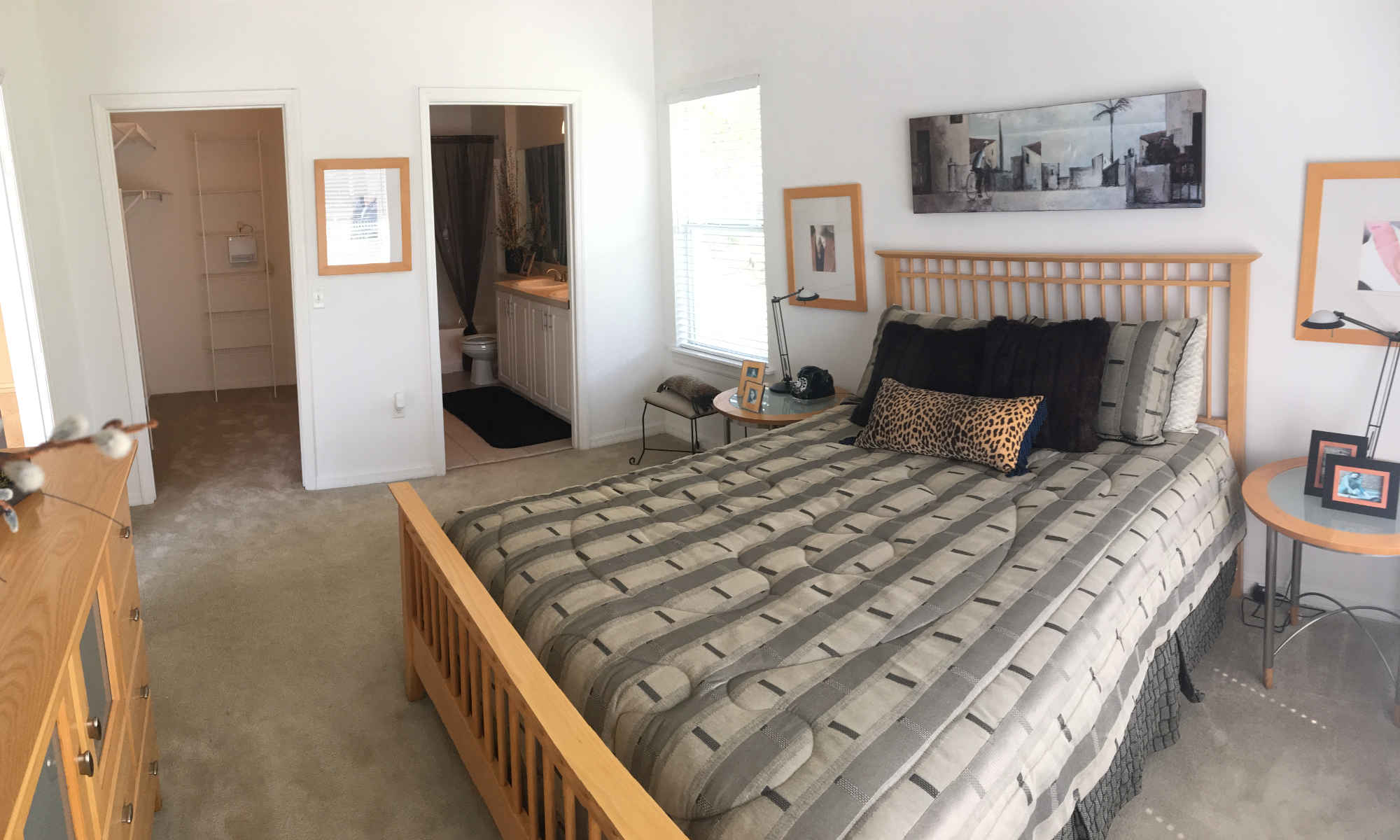 Asbury Park bedroom. Carpet. Walk-in closet and bathroom visible in background. One large window. Foreground is dominated by a queen-size bed, two end tables, and other furniture.